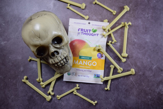 A fake skeleton head and bones lay next to a Fruit For Thought Organic Dried Mango snack pack.
