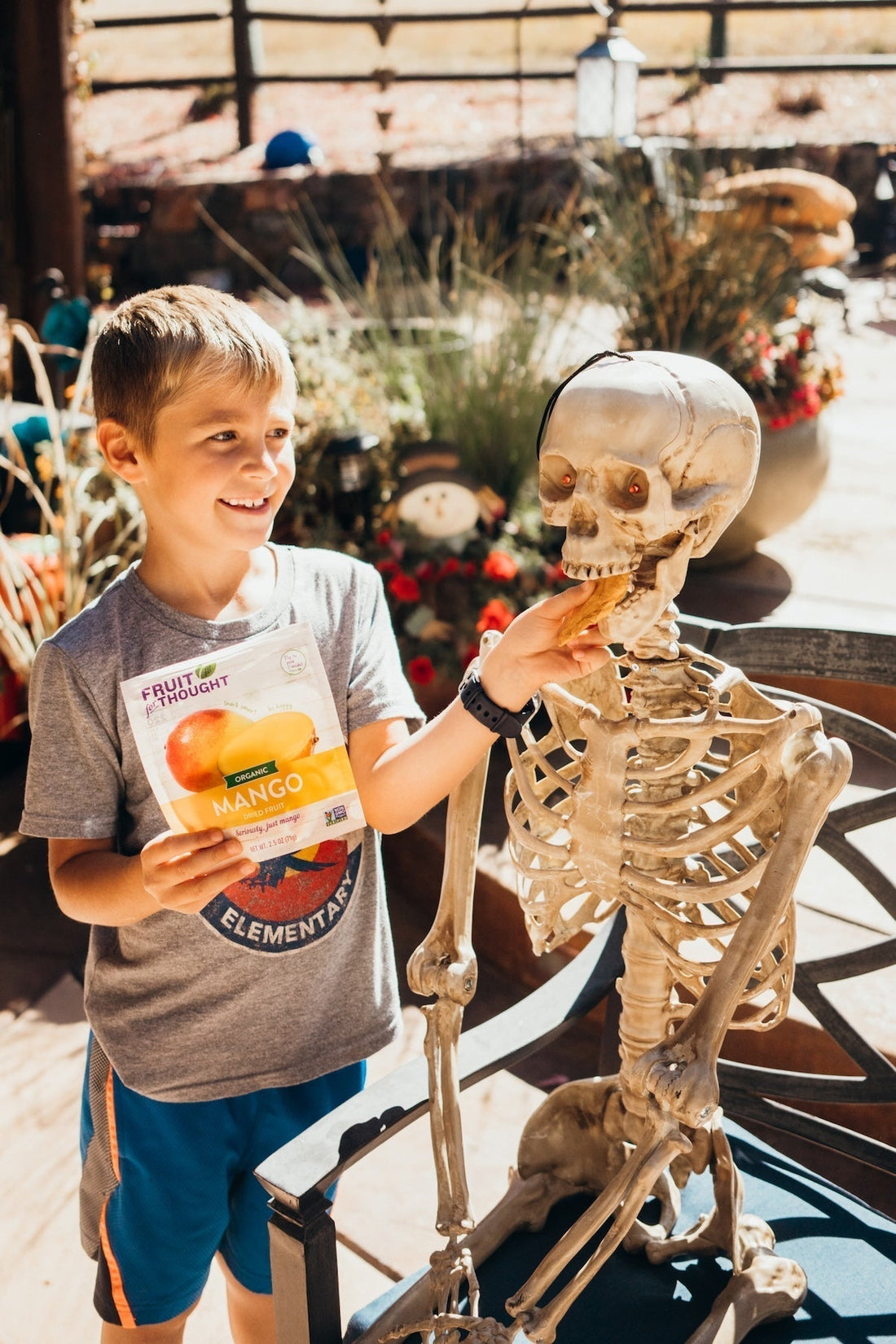 A young boy feeds a piece of dried mango to a fake skeleton.
